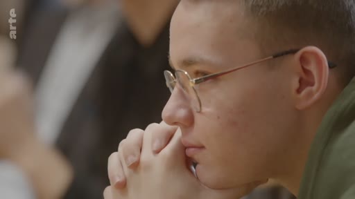 Un jeune étudiant ukrainien, portant des lunettes, écoute attentivement lors d'un débat sur les visions d'avenir pour l'Ukraine.