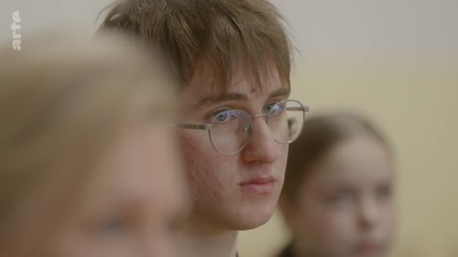 Un jeune homme aux cheveux bruns et portant des lunettes est filmé en gros plan lors d'une séquence de réflexion sur l'engagement personnel.