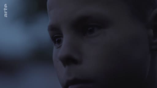 Gros plan cinématographique sur le visage d'un jeune garçon, filmé dans une lumière sombre et tamisée, évoquant une atmosphère de réflexion ou d'inquiétude.