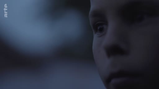 Gros plan sur le visage d'un enfant à l'expression pensive ou inquiète, filmé dans une lumière sombre et tamisée. L'image évoque une atmosphère dramatique ou introspective typique d'un documentaire ou d'une fiction.