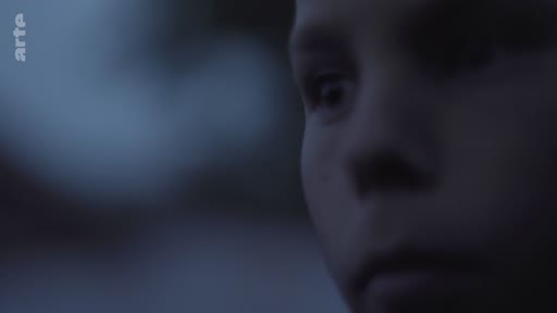 Gros plan sur le visage d'un enfant, filmé dans une lumière tamisée et sombre, évoquant une atmosphère introspective ou mélancolique.