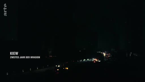 Vue nocturne d'une route à Kiev, capitale de l'Ukraine, durant la deuxième année de l'invasion russe. L'image montre la circulation automobile dans l'obscurité, illustrant la situation sécuritaire et les conditions de vie en temps de guerre.