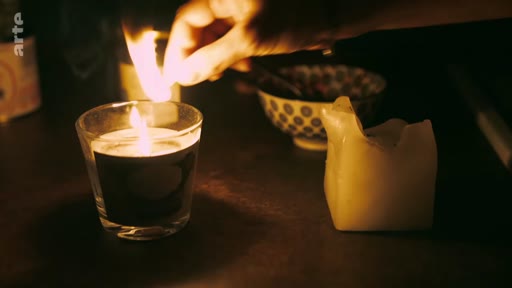 Une main allume une bougie dans un appartement sombre, illustrant une situation de précarité ou de manque d'électricité dans un appartement endommagé par la guerre.