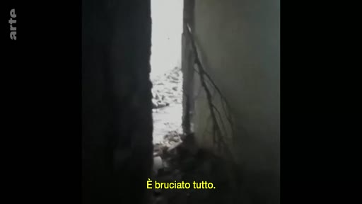 Vue intérieure montrant les conséquences d'un incendie, avec des débris et des traces de brûlures visibles à travers une ouverture. Le sous-titre indique 'È bruciato tutto', soulignant l'ampleur des destructions.