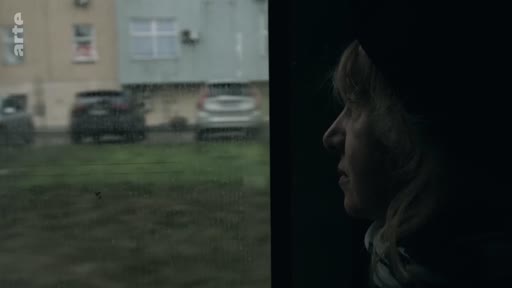 Une femme observe le paysage urbain défiler par la fenêtre d'une voiture, illustrant son voyage vers une nouvelle vie. La scène capture un moment de réflexion et de transition.