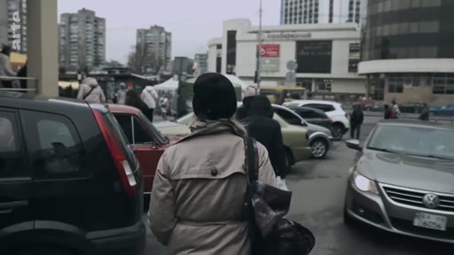 Une personne vue de dos marche dans une rue urbaine entourée de voitures, avec des bâtiments en arrière-plan.