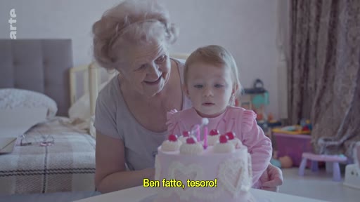 Une grand-mère et sa petite-fille célèbrent un anniversaire avec un gâteau à Kyiv, en Ukraine. La scène montre un moment de vie familiale intime dans un contexte de conflit.