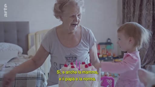 Une grand-mère et sa petite-fille partagent un moment de complicité autour d'un gâteau d'anniversaire à Kyiv, dans un contexte de vie familiale en Ukraine. La scène montre une interaction chaleureuse entre les deux générations.