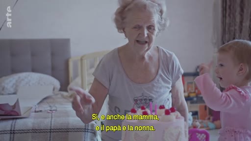 Une grand-mère et sa petite-fille partagent un moment de complicité lors d'une fête d'anniversaire à Kyiv, avec un gâteau rose sur la table. La scène illustre la vie quotidienne des familles ukrainiennes en temps de guerre.