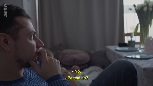 Un homme pensif est assis dans son salon, engagé dans une conversation sur la menace imminente de la guerre, comme l'indiquent les sous-titres à l'écran.