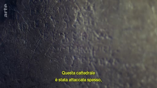 Gros plan sur une inscription ancienne gravée dans la pierre, illustrant l'histoire et les attaques subies par la cathédrale Sainte-Sophie. Le texte à l'écran souligne la vulnérabilité historique de l'édifice.