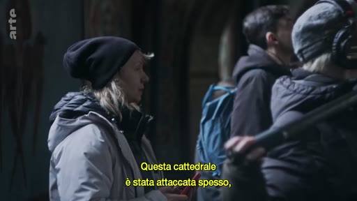 Une équipe de tournage, incluant une femme portant un bonnet noir, filme à l'intérieur de la cathédrale Sainte-Sophie. Le sous-titre mentionne les attaques répétées subies par l'édifice historique.