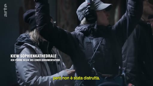 Une équipe de tournage, incluant une réalisatrice avec un casque audio, filme un documentaire à l'intérieur de la cathédrale Sainte-Sophie à Kiev. Le texte à l'écran mentionne le lieu et le contexte de la production.