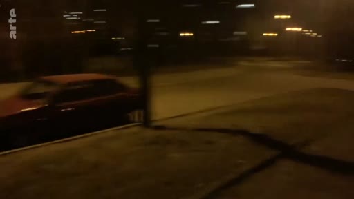 Une voiture rouge stationnée dans une rue résidentielle plongée dans l'obscurité, illustrant le climat de tension lors des premiers jours de l'invasion.