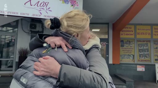 Deux personnes se serrent dans les bras lors d'un moment d'émotion devant une boutique nommée 'ХЛОЯ' en Ukraine. Cette scène illustre les départs difficiles et les retrouvailles dans un contexte de crise.