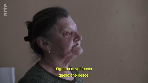 Une femme âgée, filmée en plan rapproché, livre un témoignage personnel sur le conflit. Le sous-titre indique : « Ognuna di voi faccia quello che riesce ».
