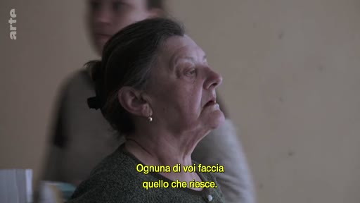 Une femme âgée s'exprime lors d'une discussion sur le conflit, avec un sous-titre en italien indiquant 'Ognuna di voi faccia quello che riesce'.