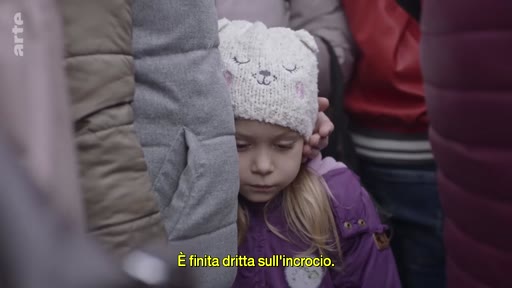 Une jeune enfant portant un bonnet à oreilles est entourée par une foule, illustrant la vie des personnes déplacées. L'image capture un moment de vulnérabilité au milieu d'un groupe de personnes.