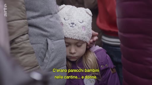 Une jeune enfant portant un bonnet à oreilles d'ours se repose contre un adulte, illustrant la détresse des civils dans les zones de conflit. L'image est accompagnée d'un sous-titre en italien évoquant la présence d'enfants et de femmes dans des caves, contexte typique des abris anti-aériens lors de la guerre en Ukraine.