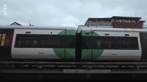 Un train de banlieue circule sur une voie ferrée, illustrant le thème des déplacements et des transports dans le cadre d'un reportage sur les parcours de réfugiés.