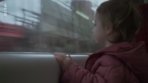 Une jeune enfant observe le paysage défiler par la fenêtre d'un train, capturant un moment de voyage et de contemplation.
