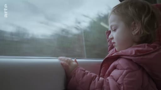 Une petite fille blonde vêtue d'une doudoune rose observe le paysage défiler depuis la fenêtre d'un train. Cette scène illustre un voyage en train avec un enfant.