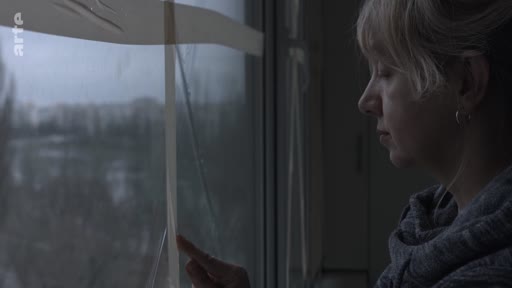 Une femme observe le paysage extérieur à travers une fenêtre, son doigt posé sur une bande adhésive apposée sur la vitre, dans une ambiance mélancolique et intimiste.