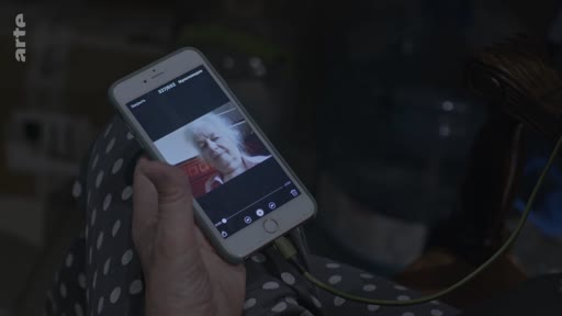 Une personne tient un smartphone affichant une vidéo d'une femme âgée, illustrant une communication à distance ou un appel vidéo.