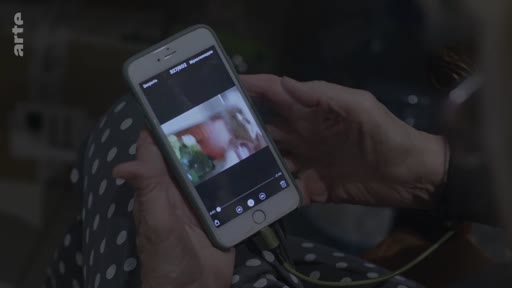 Une personne âgée tient un smartphone entre ses mains pour visionner une vidéo, illustrant l'usage des technologies numériques au quotidien.