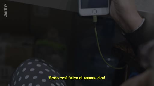 Une personne tient un smartphone en main pour un appel vidéo, avec le sous-titre italien affiché à l'écran : 'Sono così felice di essere viva!'.