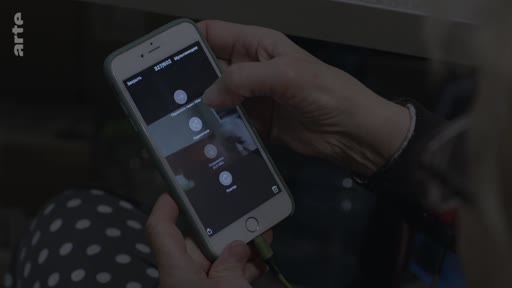 Une personne manipule un smartphone affichant une interface d'application avec des icônes circulaires, dans le contexte d'un reportage sur la situation à Marioupol.