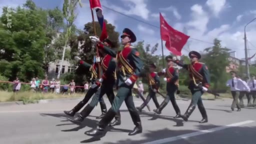 Des soldats en uniforme défilent avec des drapeaux lors d'une parade militaire organisée par les forces russes dans la ville occupée de Marioupol, en Ukraine.