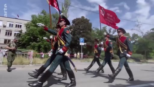 Des soldats russes en uniforme de parade défilent dans les rues de Marioupol, portant des drapeaux, lors d'une cérémonie militaire organisée par les forces russes dans la ville occupée.