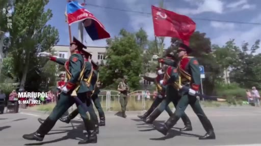 Des soldats en uniforme défilent dans les rues de Marioupol le 9 mai 2022, portant des drapeaux russes et soviétiques lors d'une parade militaire organisée dans la ville occupée.