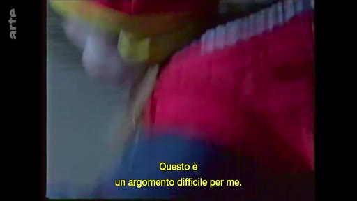 Une femme, dont le visage est partiellement visible, s'exprime sur un sujet personnel ou difficile, comme l'indique le sous-titre en italien à l'écran.