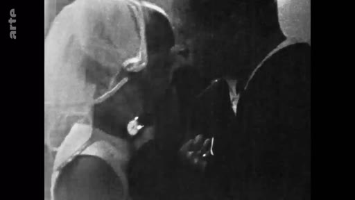 Image d'archive en noir et blanc montrant une femme en robe de mariée avec un voile, lors d'une cérémonie de mariage.