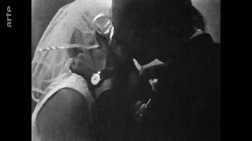 Une image d'archive en noir et blanc montrant un couple en tenue de mariage s'embrassant tendrement. La mariée porte un voile et une montre, capturant un moment intime et nostalgique.