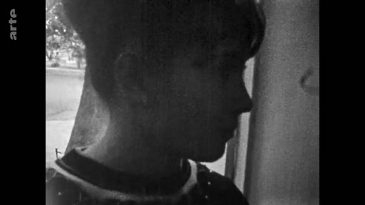 Portrait en gros plan d'une jeune fille filmée en noir et blanc, évoquant une séquence d'archives personnelles ou familiales.