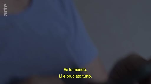 Une personne en t-shirt bleu discute en montrant des photographies à un membre de sa famille, avec des sous-titres en italien à l'écran.