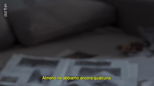 Des photographies en noir et blanc sont disposées sur un canapé, illustrant une discussion sur des souvenirs ou des archives familiales. Le sous-titre indique : « Almeno ne abbiamo ancora qualcuna ».