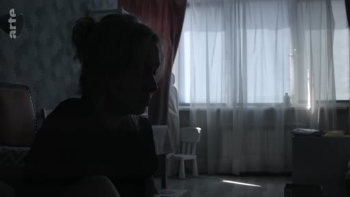 Une femme est filmée en contre-jour dans une pièce intérieure, créant une silhouette sombre. L'ambiance est calme et mélancolique, évoquant un moment d'introspection ou d'écoute.