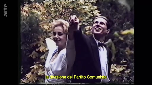 Un jeune couple en tenue de soirée, l'homme en smoking et la femme en robe claire, pose ensemble dans un jardin arboré. L'image est accompagnée d'une légende faisant référence à la direction du Parti communiste.