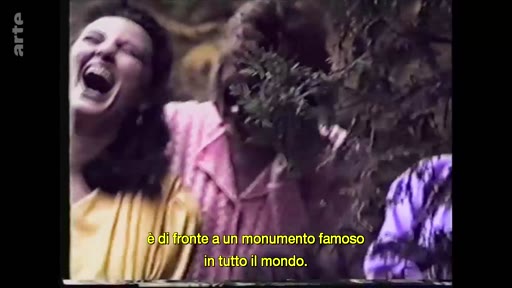 Des personnes rient joyeusement devant un monument célèbre, comme l'indique le sous-titre à l'écran. Cette image d'archive illustre une scène de vie quotidienne ou touristique.