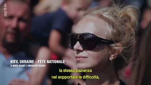 Une femme blonde portant des lunettes de soleil est filmée lors de la fête nationale à Kiev, six mois avant l'invasion russe de l'Ukraine. Elle est entourée par la foule lors de cet événement public.