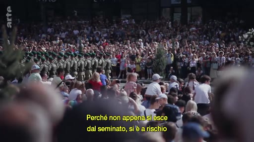 Une foule nombreuse assiste à un défilé militaire en extérieur, avec des soldats en uniforme marchant au pas. Le sous-titre souligne les risques liés à la sortie du cadre établi.