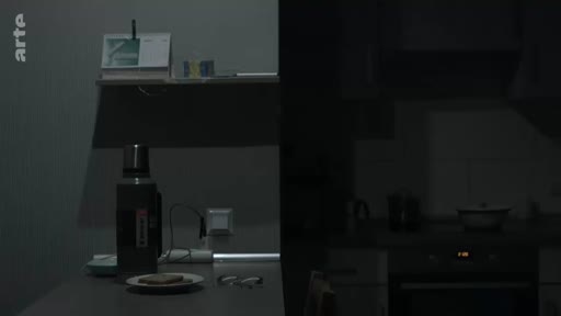 Vue intérieure d'une cuisine plongée dans l'obscurité à Marioupol, illustrant les conditions de vie précaires durant le conflit. On distingue une bouteille isotherme et une assiette sur une table, témoignant du quotidien des habitants sous les bombardements.