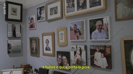 Un mur intérieur orné d'une collection de portraits photographiques de famille, illustrant une atmosphère personnelle et chaleureuse. Le texte à l'écran évoque l'esprit de Noël.