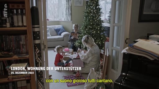 Une famille célèbre Noël dans leur appartement à Londres le 25 décembre 2022, avec un sapin de Noël décoré et des cadeaux. La scène montre une ambiance festive et domestique.