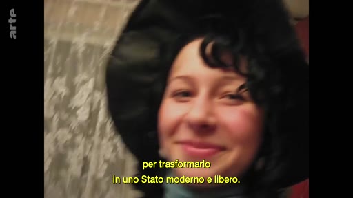 Une jeune femme souriante, coiffée d'un chapeau noir, apparaît à l'écran lors d'une séquence filmée, probablement dans le cadre d'un reportage sur le Nouvel An à Marioupol. Le sous-titre en italien évoque la transformation en un État moderne et libre.