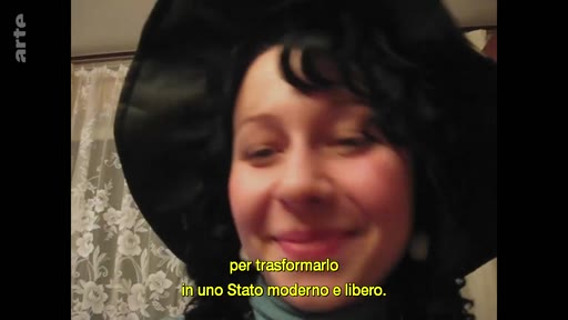 Une femme souriante, coiffée d'un chapeau noir, s'exprime lors d'une interview. Le sous-titre en italien mentionne la transformation en un État moderne et libre.